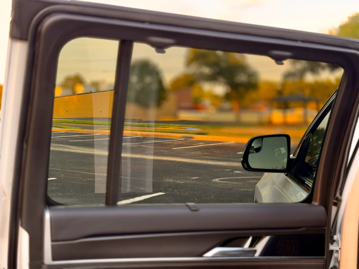 View through an open car window showing a parking lot and side mirror.