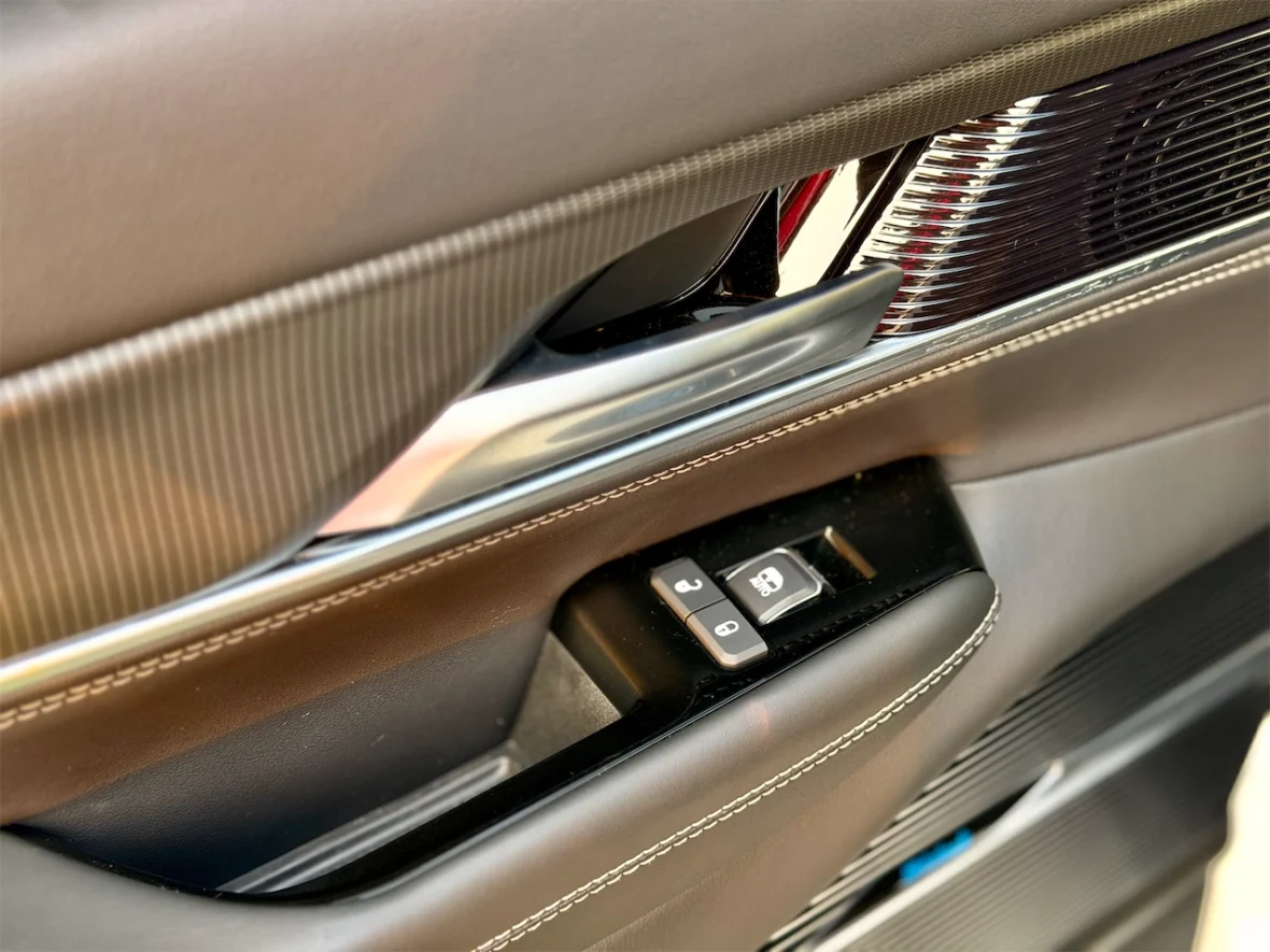 Close-up view of a car door panel featuring a chrome handle, window control buttons, and textured leather accents.