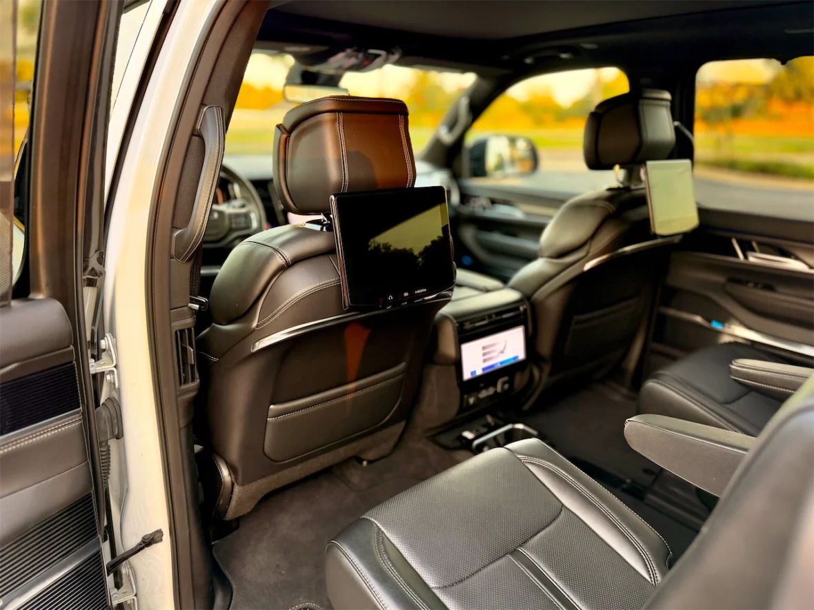 Interior view of a luxury vehicle showcasing black leather seats, with a rear entertainment tablet mounted on the headrest and control panel visible in the center console.