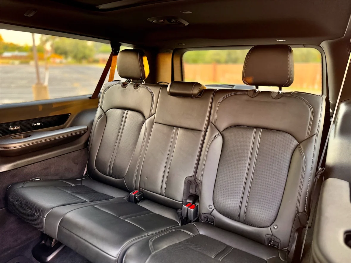 Interior view of a spacious back seat in a vehicle, featuring black leather upholstery and headrests, with a visible window showing a blurred outdoor background.
