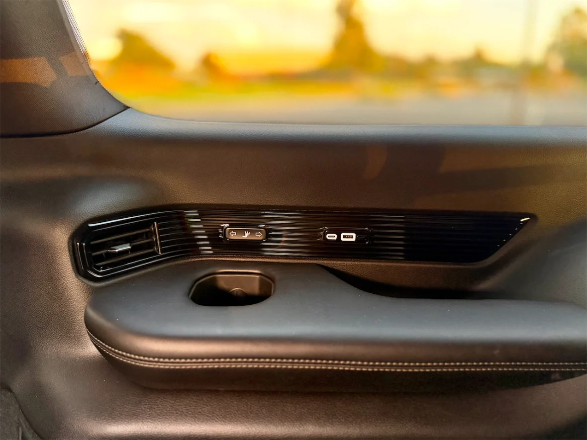 Interior door panel of a vehicle showing window control buttons, air vent, and a storage compartment.