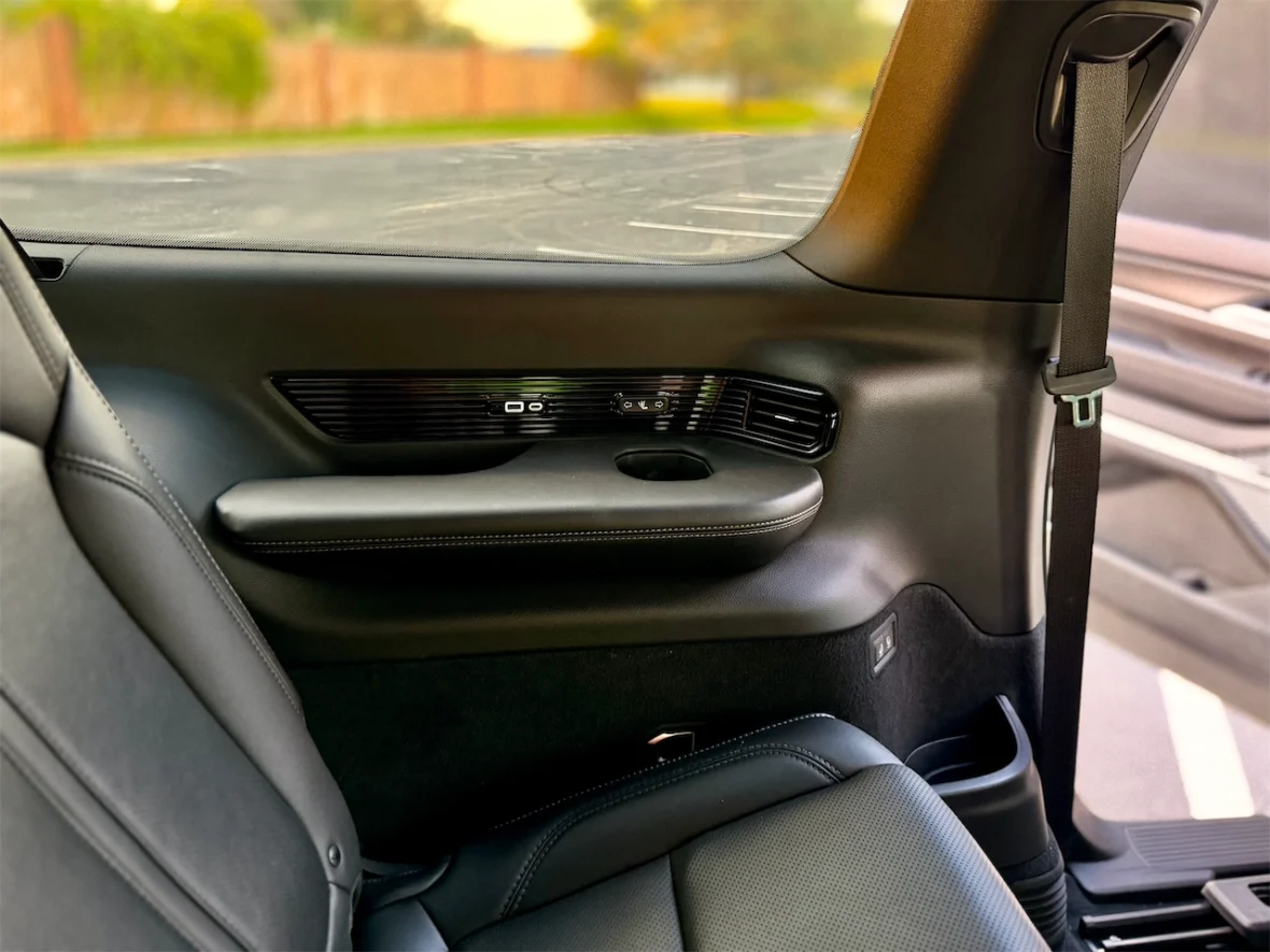 Interior view of a vehicle's back seat, showcasing the door panel with controls and a smooth leather seat.