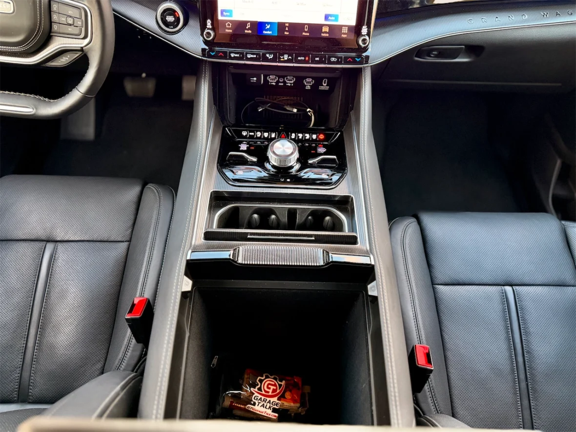 Interior view of a modern car showing the center console, featuring a touchscreen display, gear shift, and cup holders. The seats are upholstered in black leather.