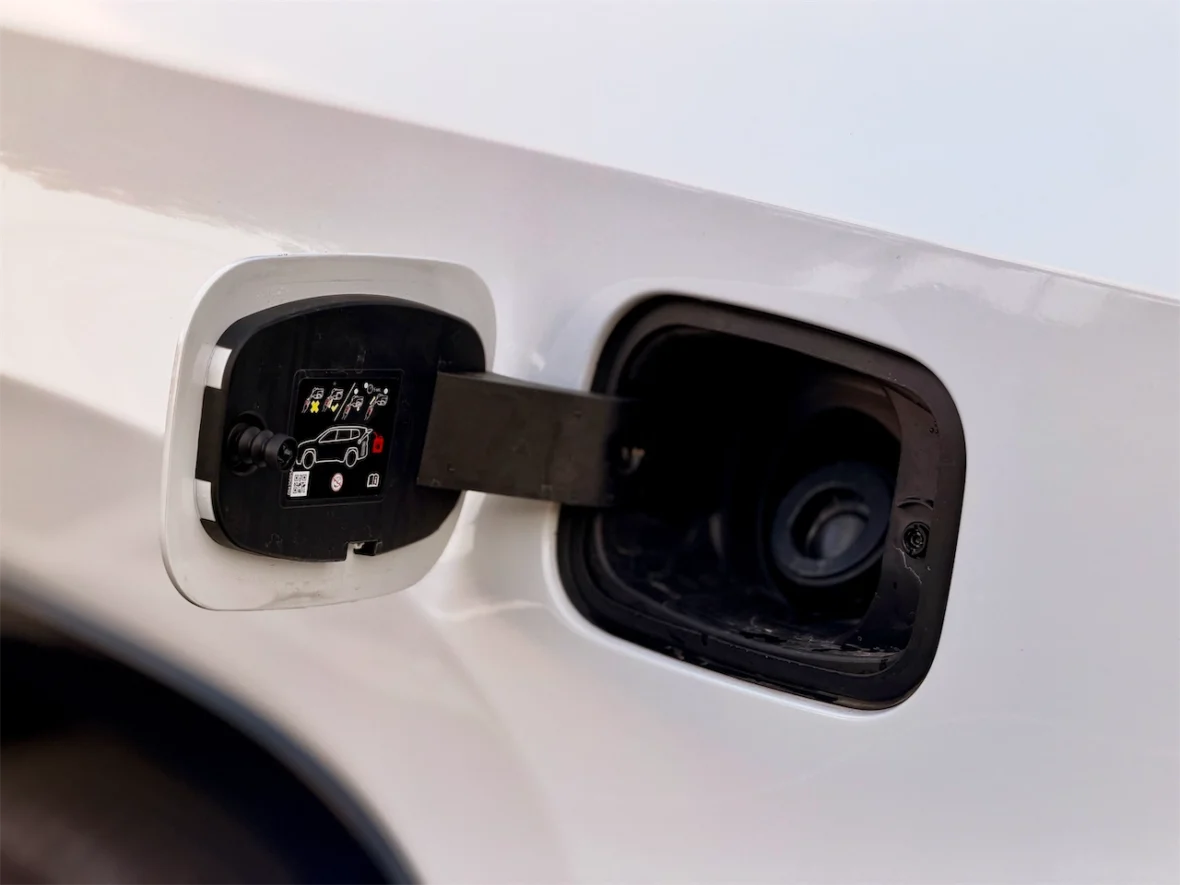 Close-up of a vehicle's fuel door showing the release mechanism and warning labels.