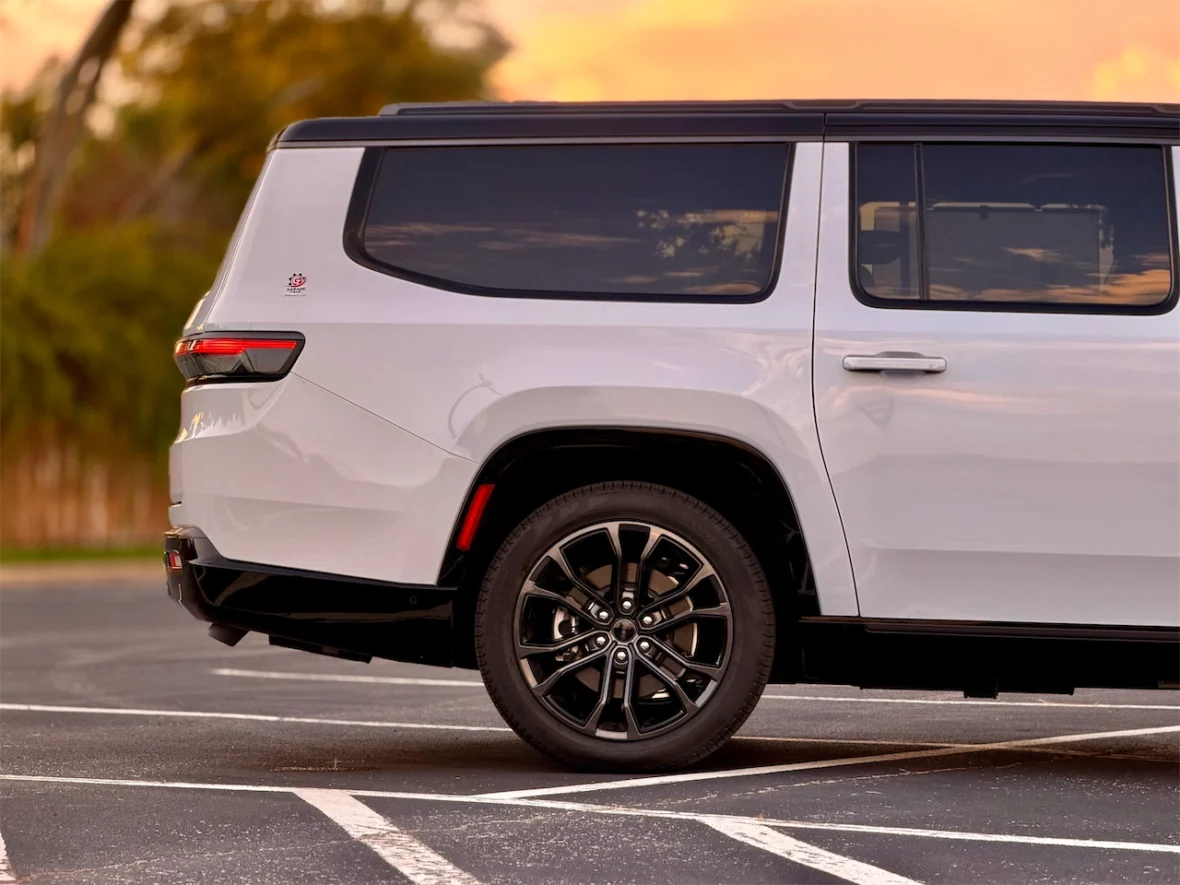 Side view of the 2026 Jeep Grand Wagoneer L parked in a lot with a sunset backdrop, showcasing its sleek design and black alloy wheels.