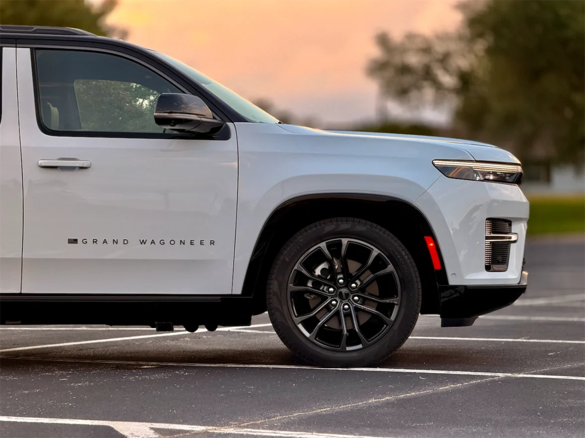 Side view of a white Grand Wagoneer SUV with black wheels parked in a lot during sunset.