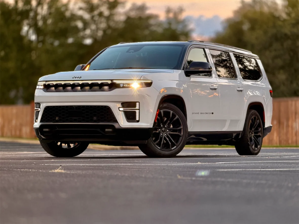 The 2026 Jeep Grand Wagoneer L parked in a lot with trees in the background, showcasing its sophisticated design and black wheels.