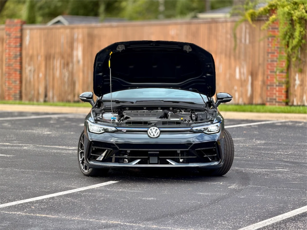 Front view of a Volkswagen car with the hood open, showcasing the engine bay in a parking lot.