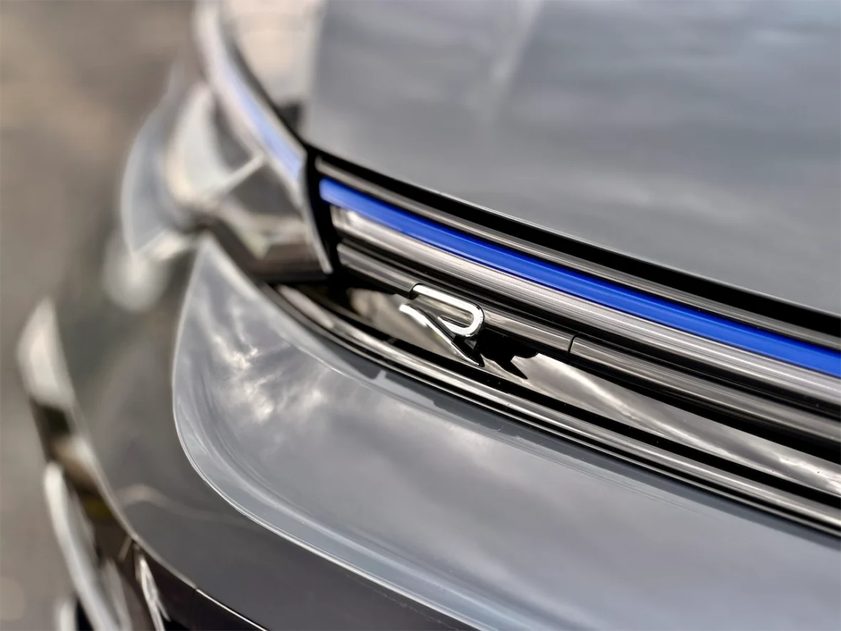 Close-up of a car's front grille featuring a sleek design with a blue accent and a prominent 'R' logo.