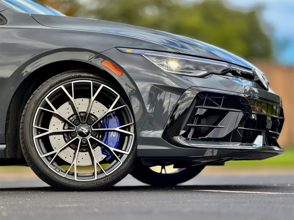 Close-up of a sports car's front wheel, showcasing a sleek gray finish, intricate black alloy wheel design, and visible blue brake calipers.