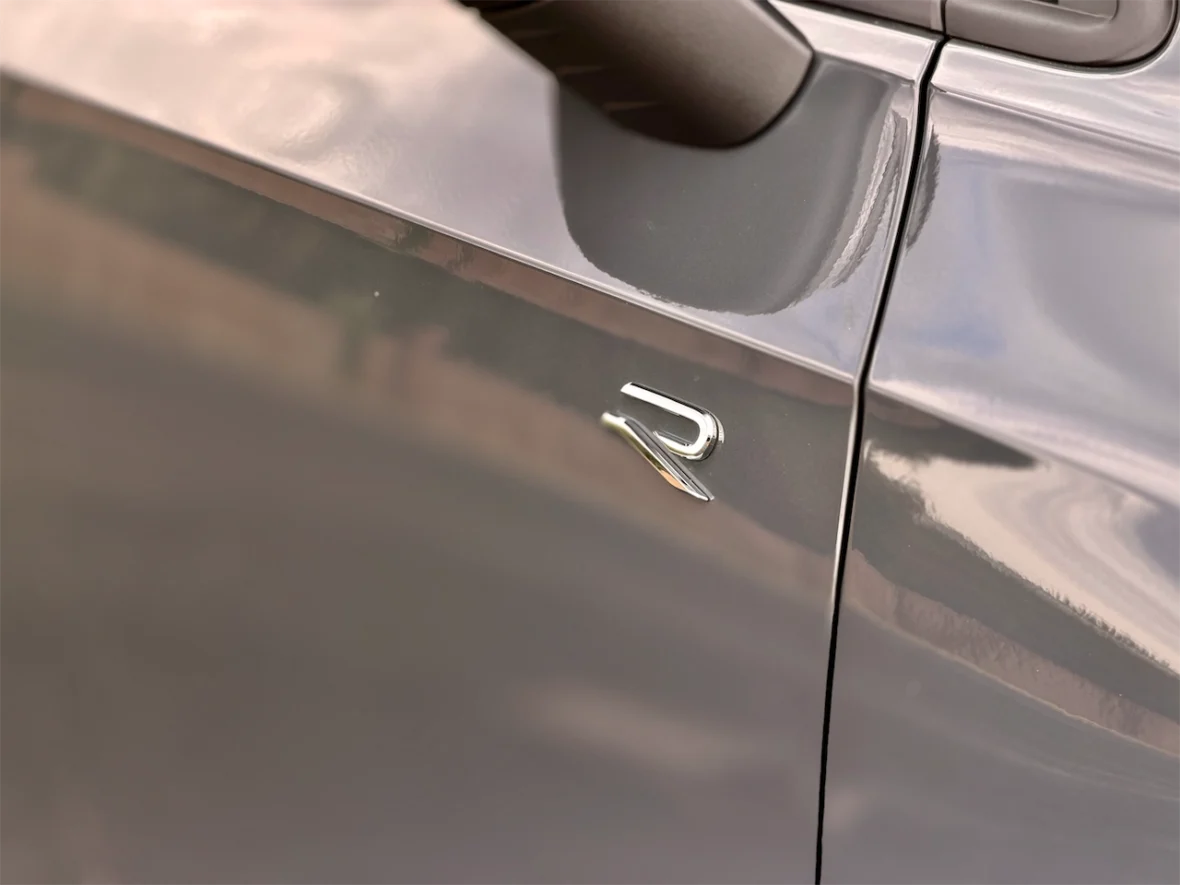Close-up of a car door featuring a shiny 'R' badge.