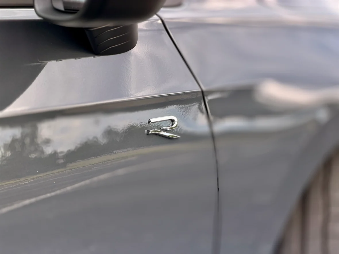 Close-up of a car door featuring a silver 'R' badge on a sleek grey surface.
