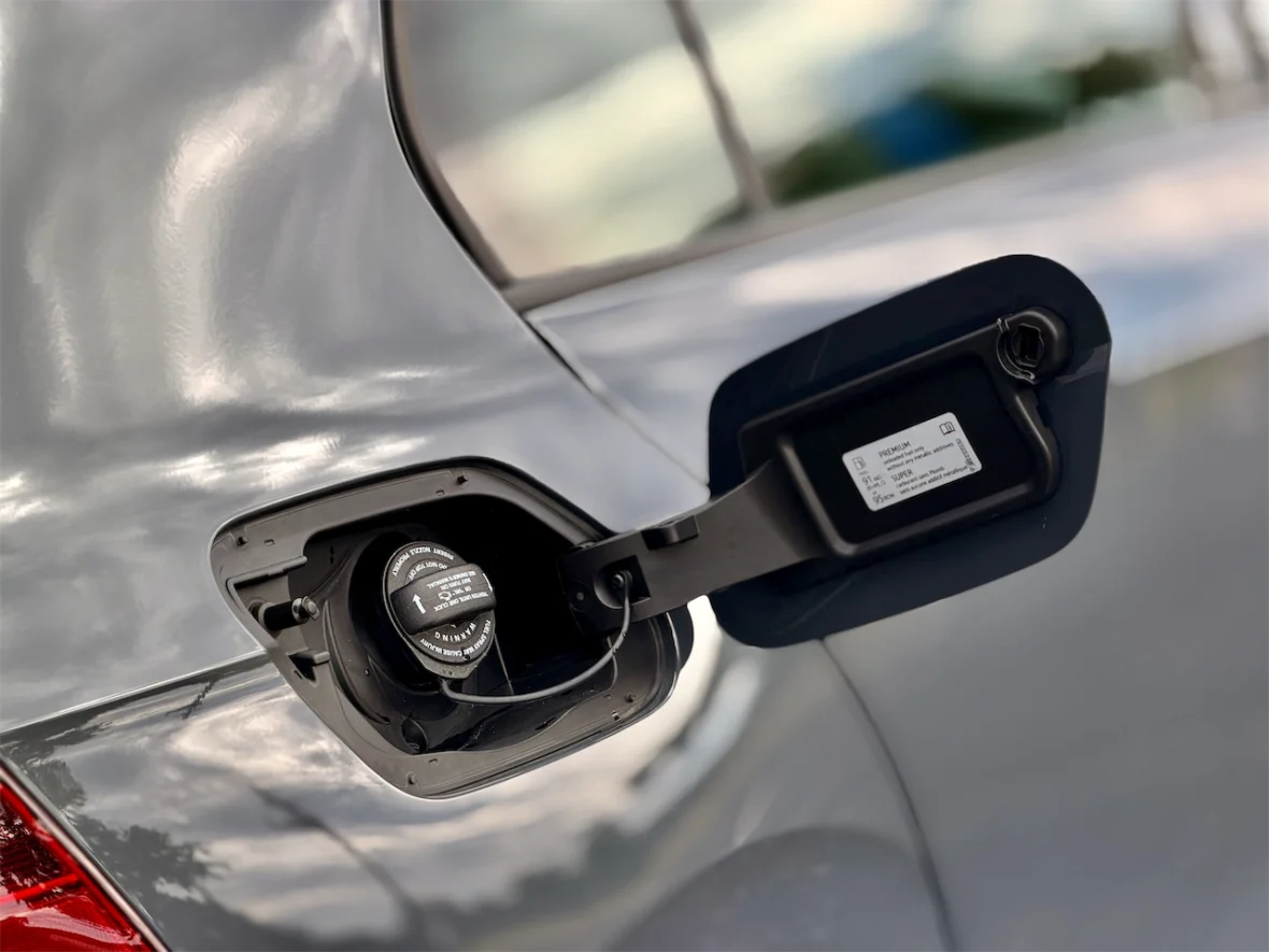 Close-up of a car's fuel filler door with a gas cap, showcasing fuel specifications and a reflective metallic surface.