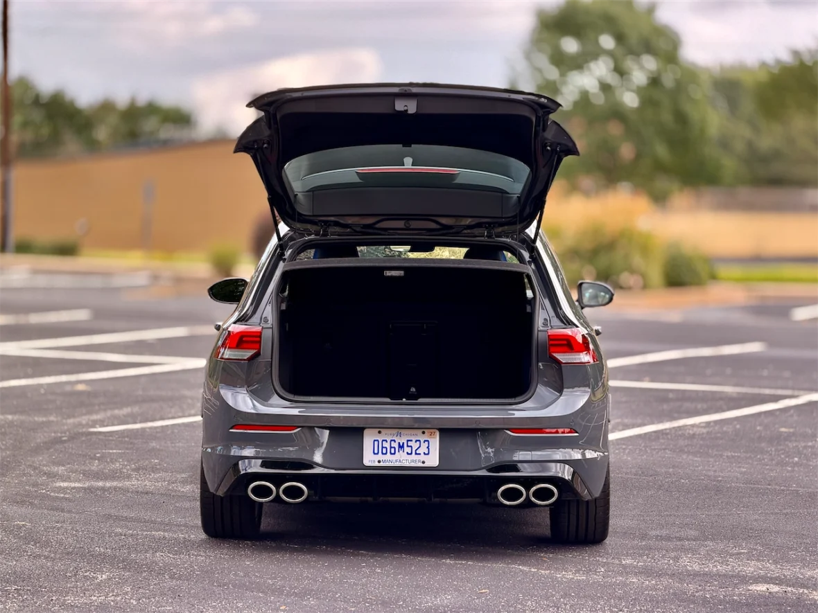 Rear view of a gray car with its trunk open, parked in a lot with no other cars visible.