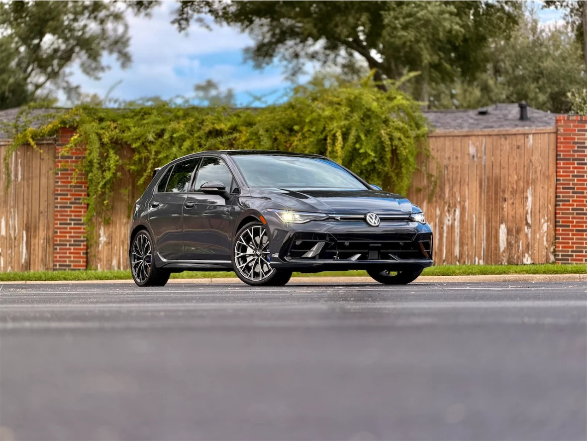 A black Volkswagen car parked on a street with a wooden fence in the background.