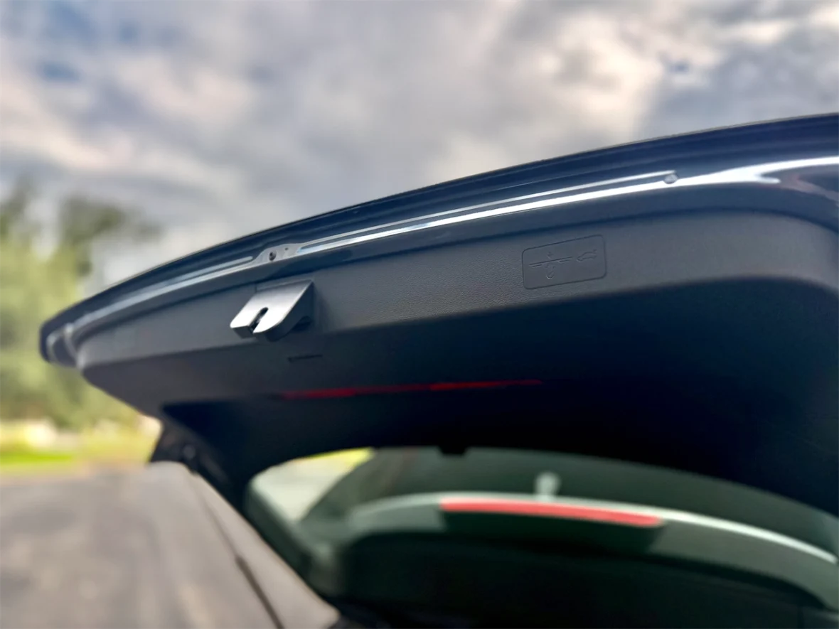 Close-up of the interior of a car trunk, focusing on the trunk lid's latch and an adjacent warning label.