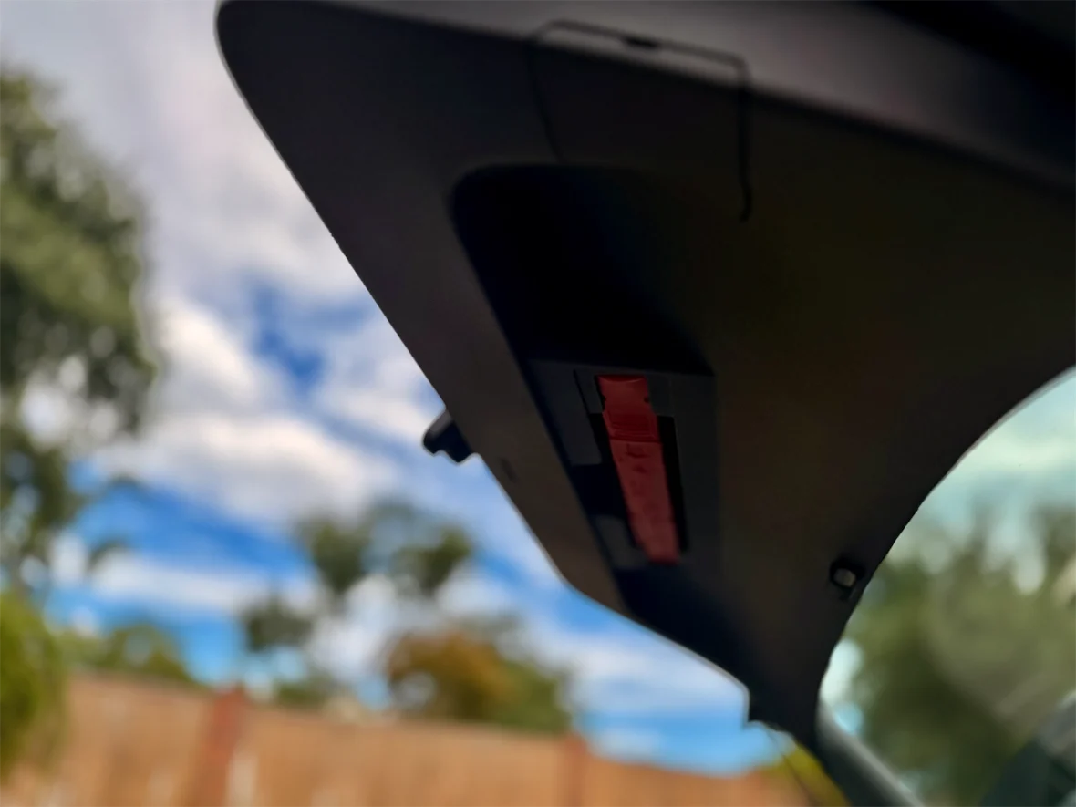 Close-up view of the interior of a car showing the roof console near the windshield, with a clear sky and trees in the background.