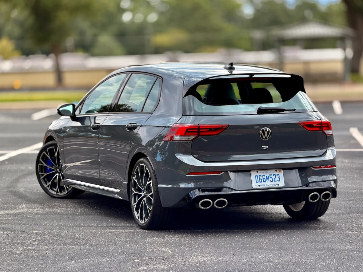 Rear view of a gray Volkswagen Golf R parked in an outdoor lot, showcasing its sporty design and dual exhaust pipes.