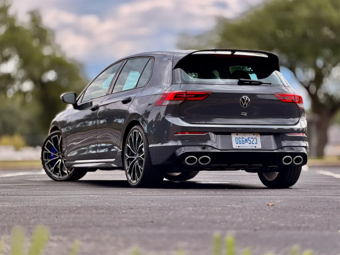 A rear view of a gray Volkswagen Golf R parked in an outdoor setting, showcasing its sleek design and sporty features.