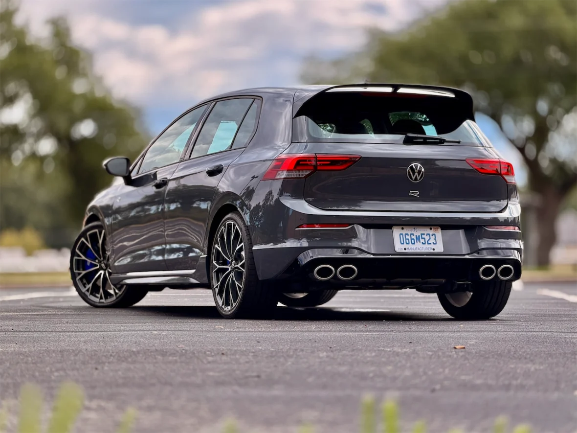 A sleek gray Volkswagen Golf R parked, showcasing its sporty design, rear view with distinctive exhaust pipes, and stylish alloy wheels against a blurred natural background.