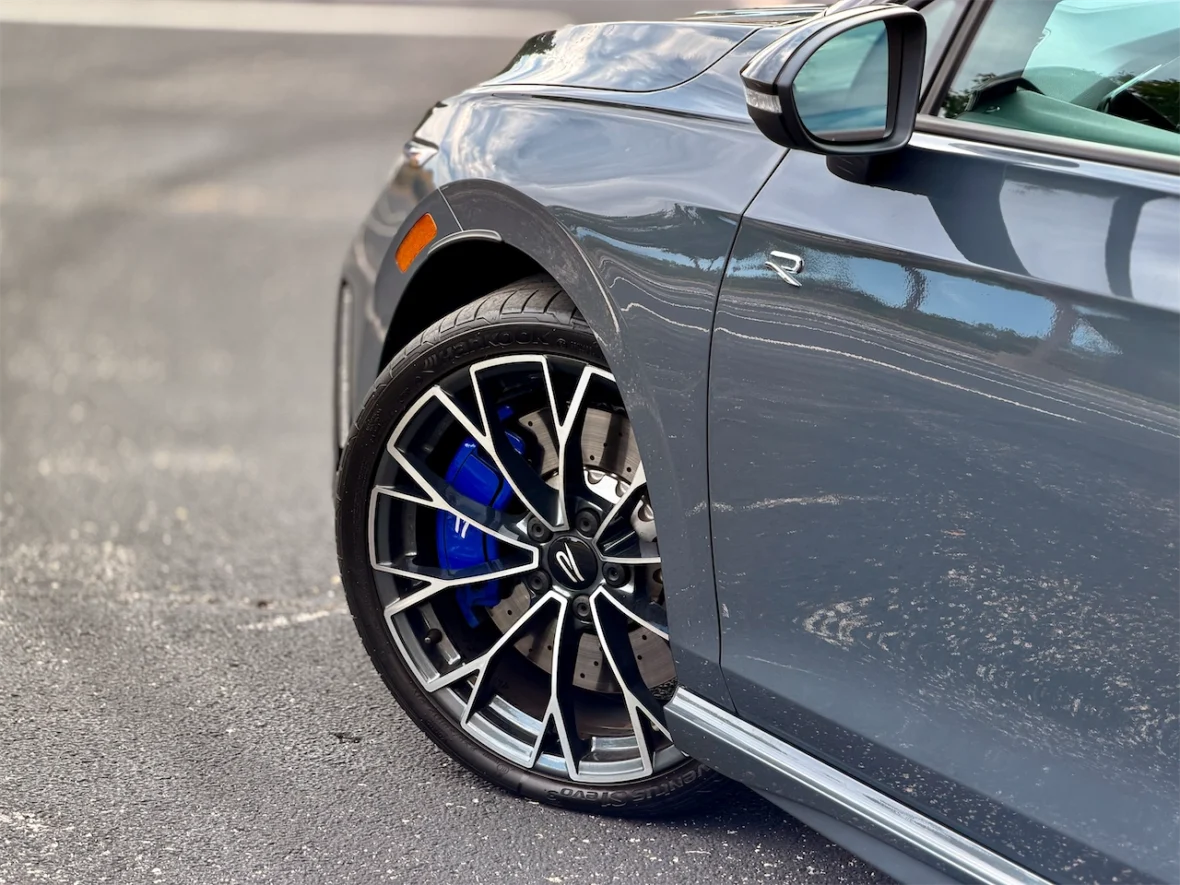Close-up of a stylish car wheel with a black and silver design, featuring blue brake calipers, parked on a smooth asphalt surface.