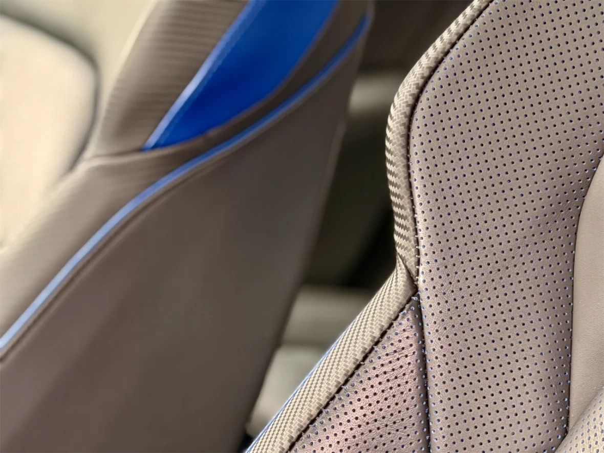 Close-up of modern car seats showing beige perforated leather with blue accent stitching.
