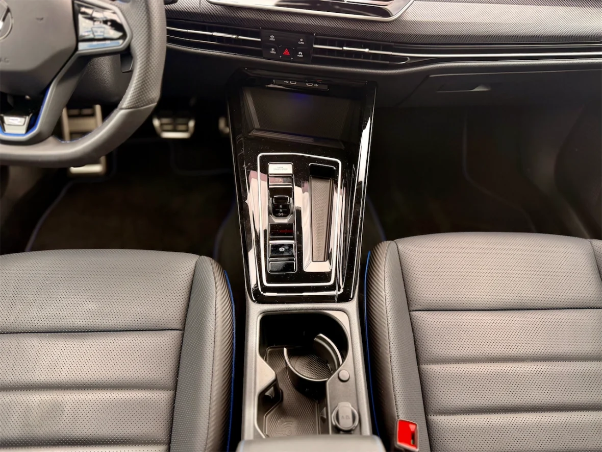 Overhead view of a car interior featuring a leather steering wheel, a central console with control buttons, and two front seats with textured upholstery.