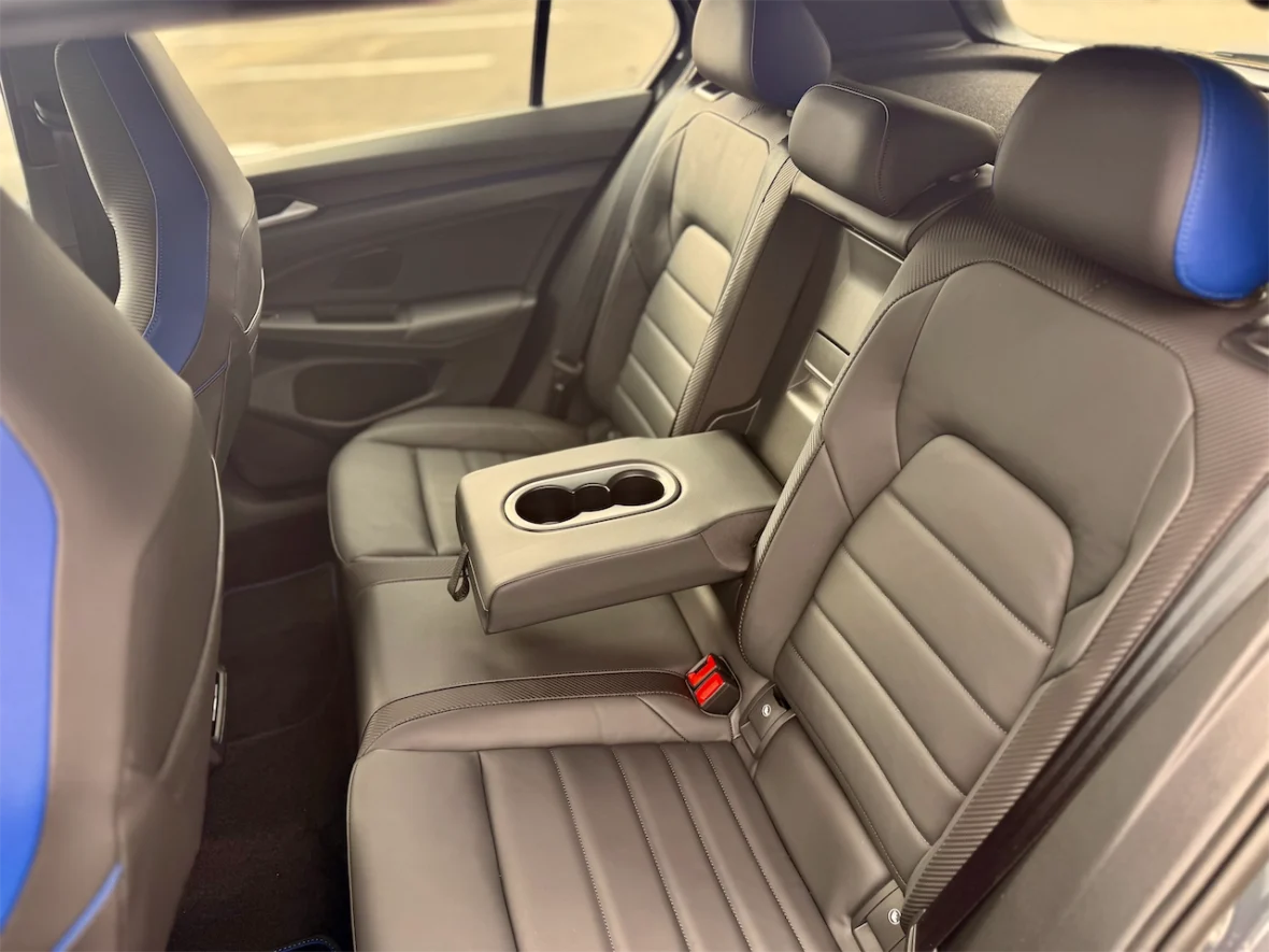 Interior view of a car's back seat featuring two seating areas with grey leather upholstery and blue accents, along with a central armrest that includes cup holders.