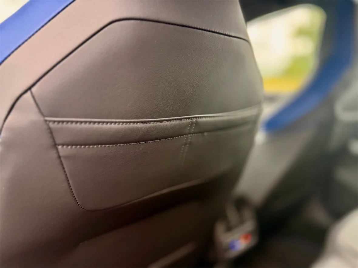 Close-up of a car seat backrest, showcasing black leather upholstery with a decorative stitch and a small pocket.