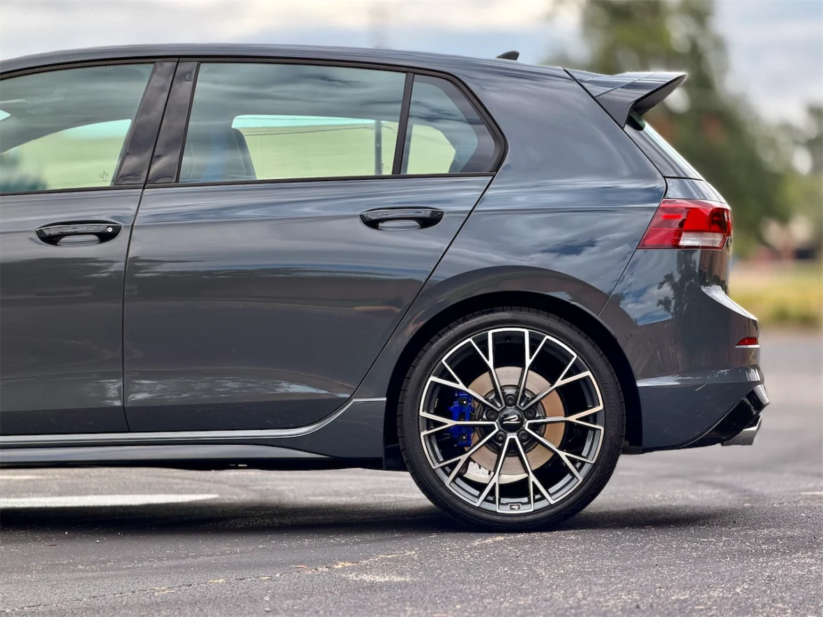 Side view of a gray hatchback car showing sleek design, prominent rear spoiler, and stylish alloy wheels.