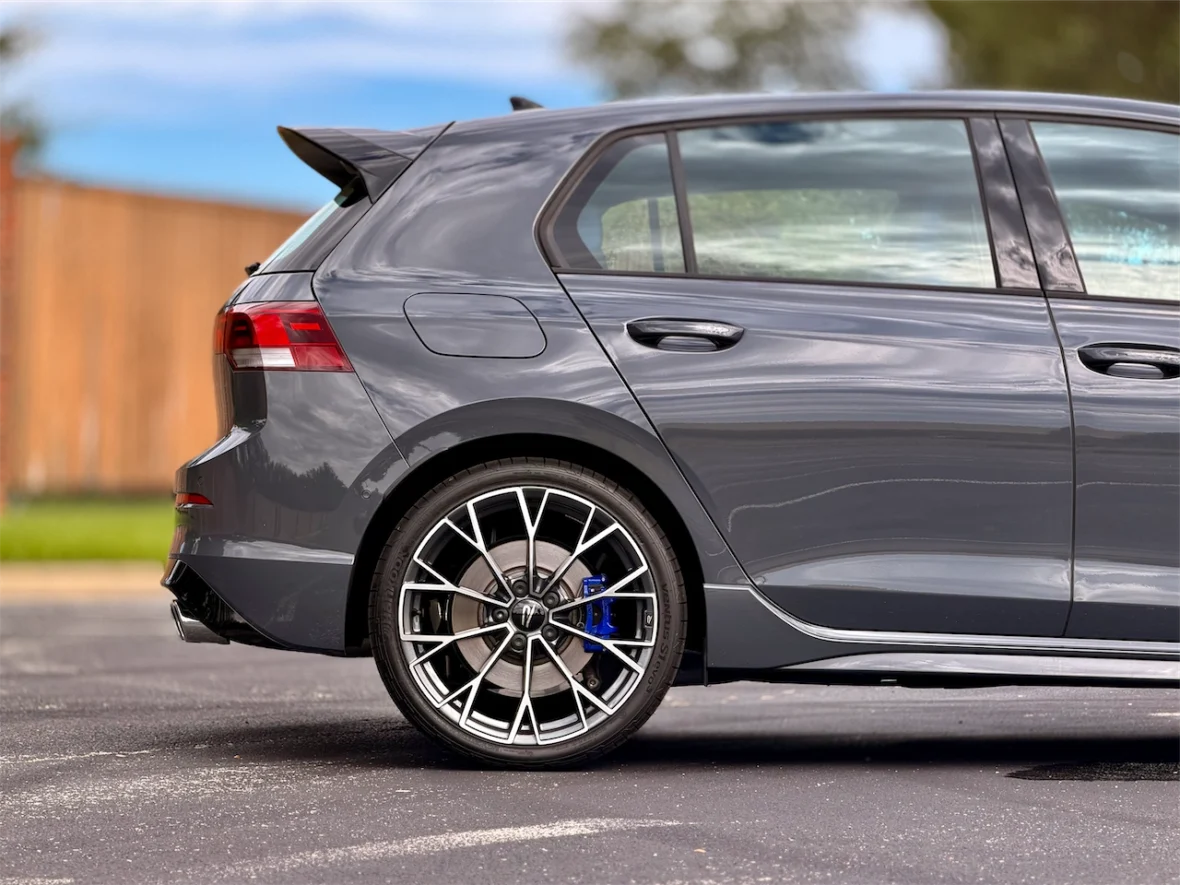 Side view of a gray sporty car with a sleek design and alloy wheels, parked on a black surface.