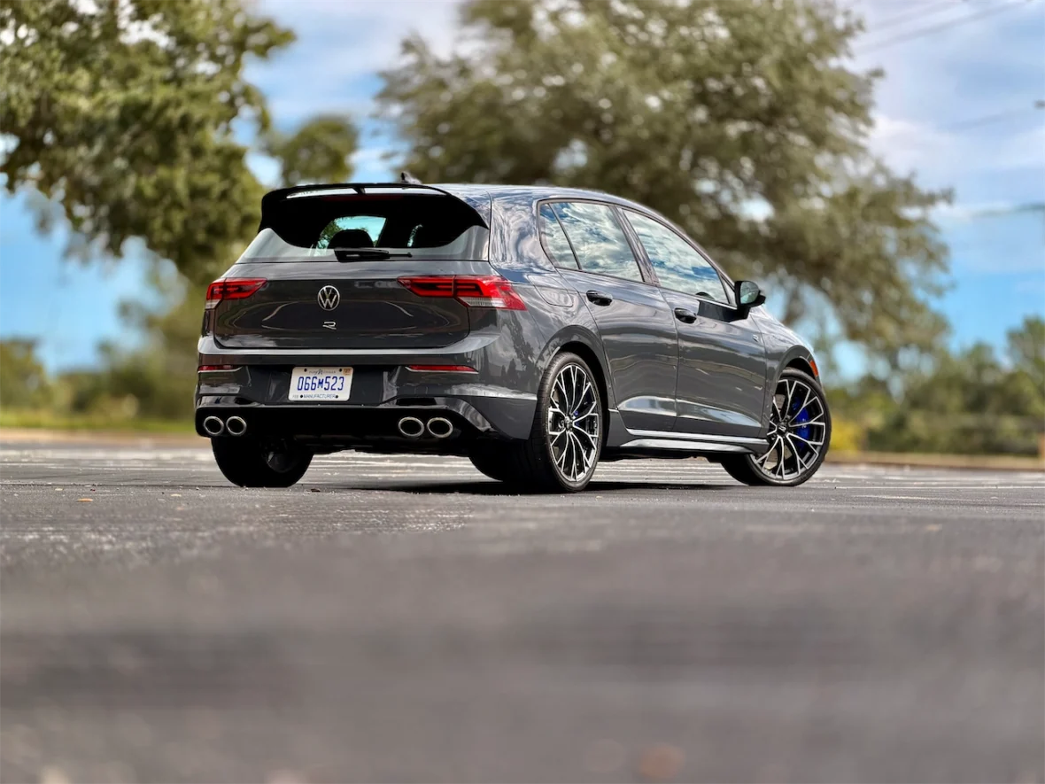 A sleek gray Volkswagen hatchback parked at an empty lot, showcasing its sporty design and distinctive rear features, including a rear spoiler and quad exhaust pipes.