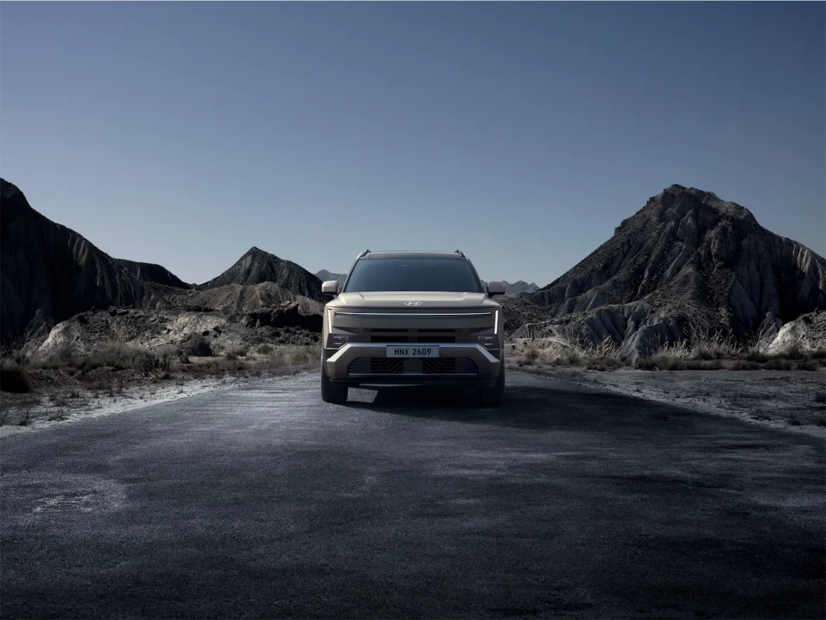 A front view of a modern SUV parked on a deserted road, surrounded by rugged mountains and a clear blue sky.
