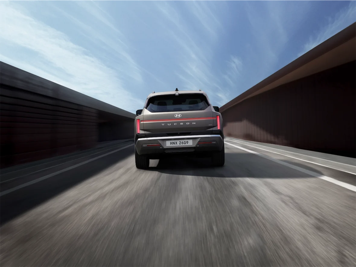 Rear view of a Hyundai Tucson driving on a road with a blue sky and minimal clouds in the background.