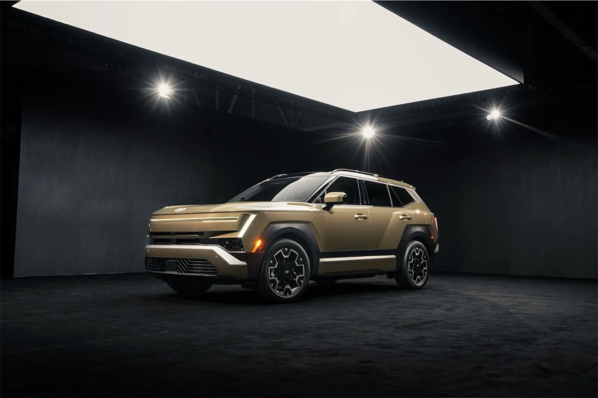 A modern SUV in a gold finish, showcased in a dimly lit exhibition space with dramatic lighting.