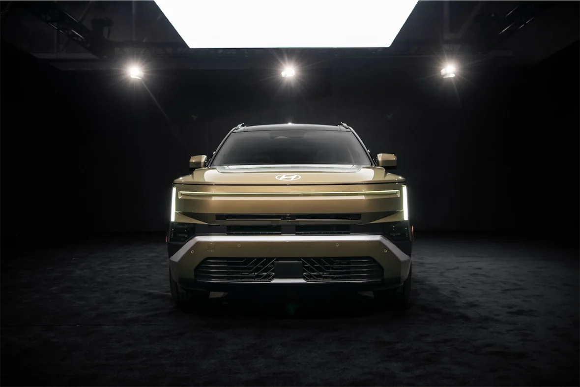 Front view of a modern SUV with a sleek design and distinctive LED headlights, showcased in a dimly lit environment.