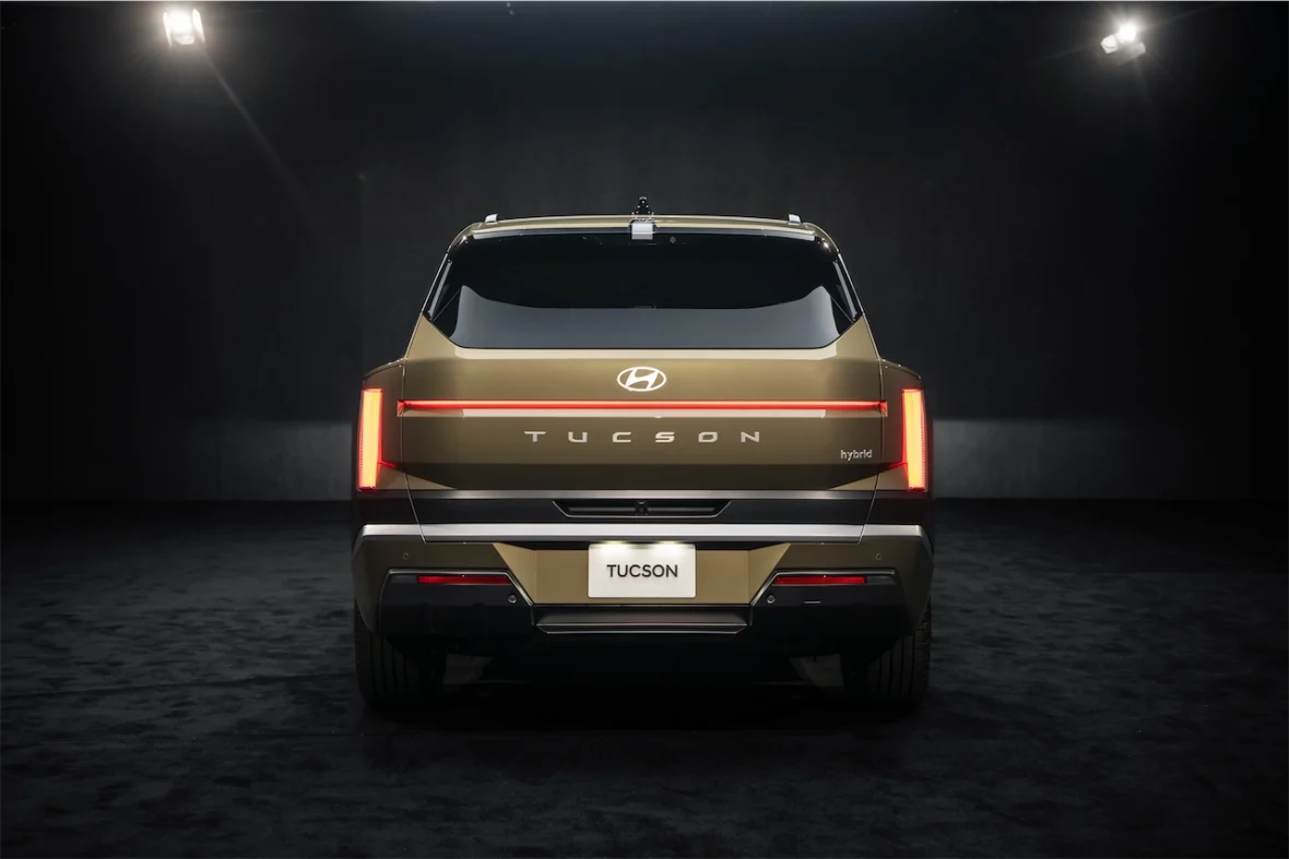 Rear view of a Hyundai Tucson hybrid vehicle, showcasing its modern design and distinctive rear lights against a dark background.