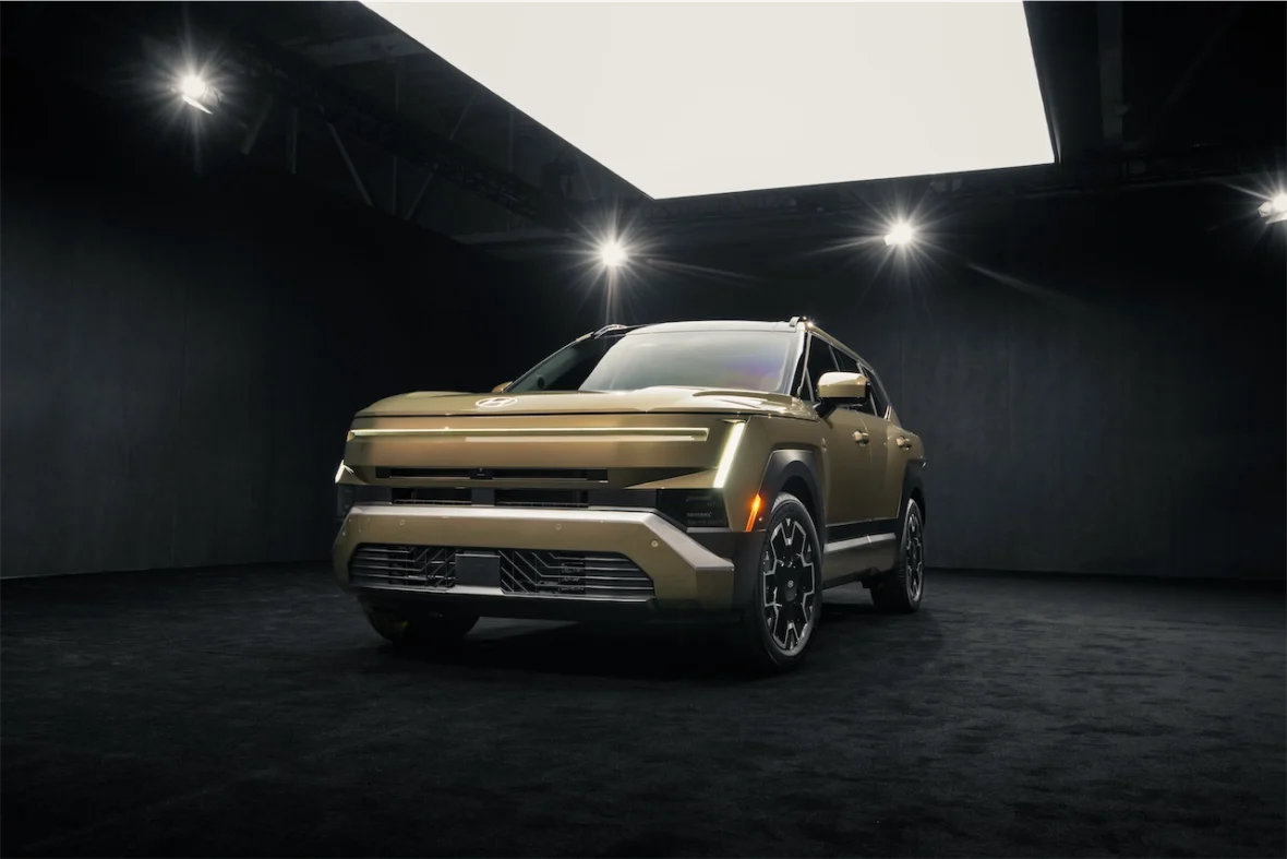 Front view of a modern SUV in a dark exhibition space, showcasing a sleek design with a distinctive bold color and unique lighting.