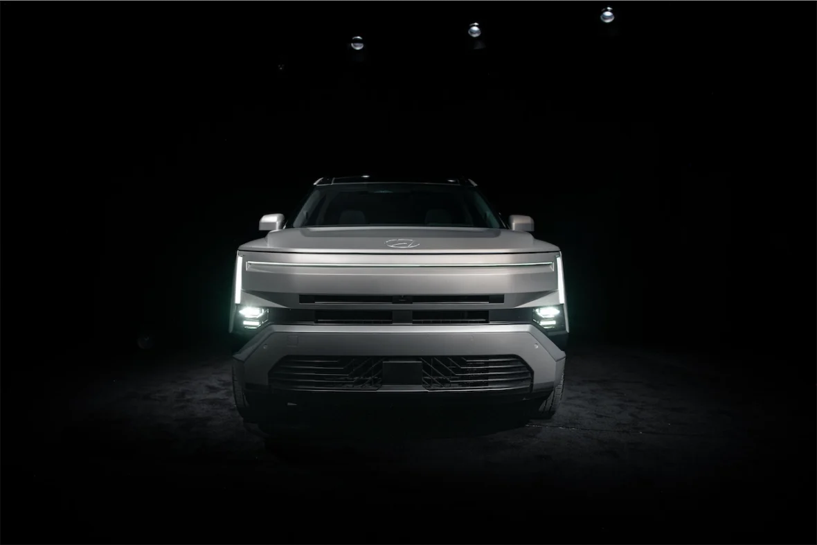 Front view of a modern electric pickup truck with a sleek design, illuminated headlights, and a dark background.