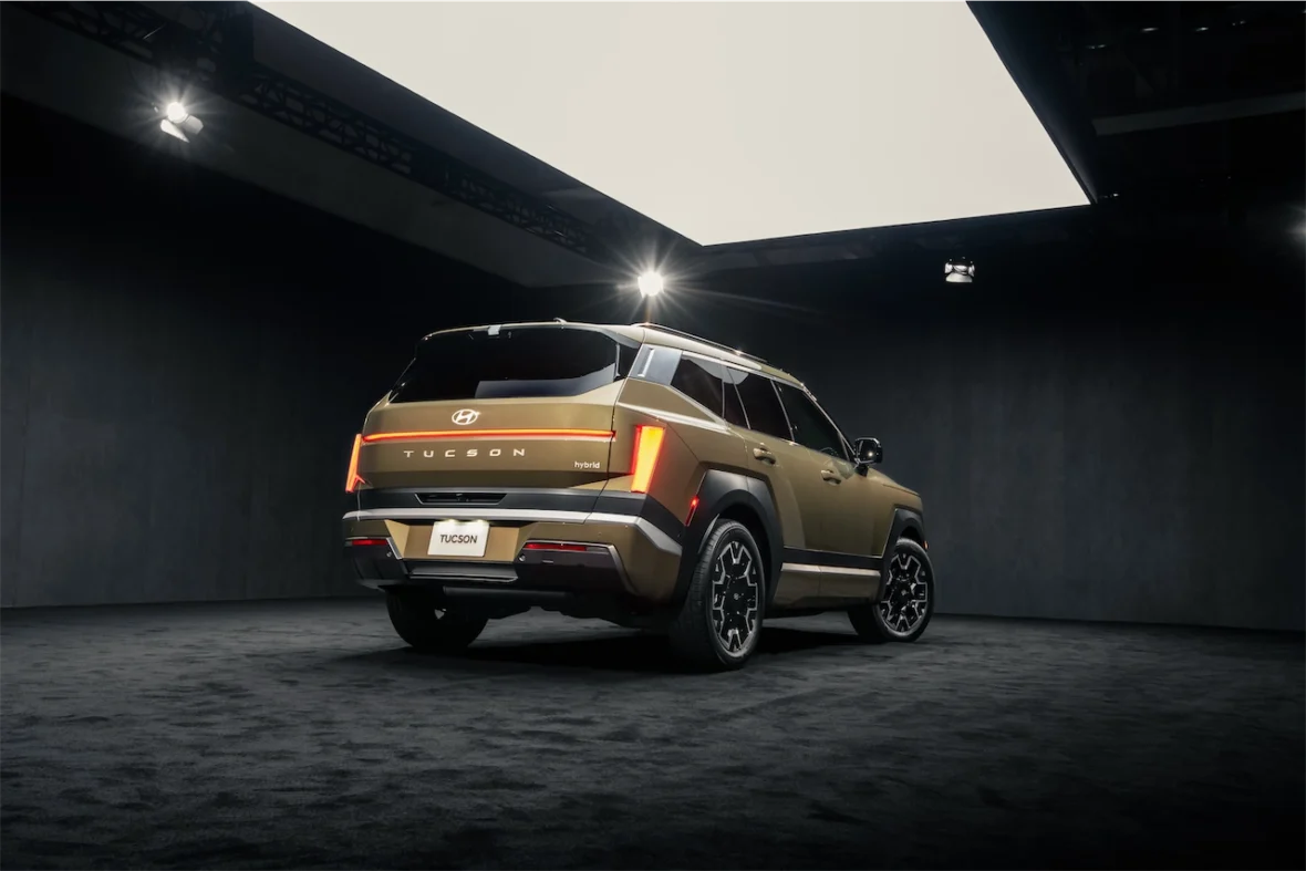 A rear view of a Hyundai Tucson hybrid SUV displayed in a modern showroom with a dark background and spotlighting.
