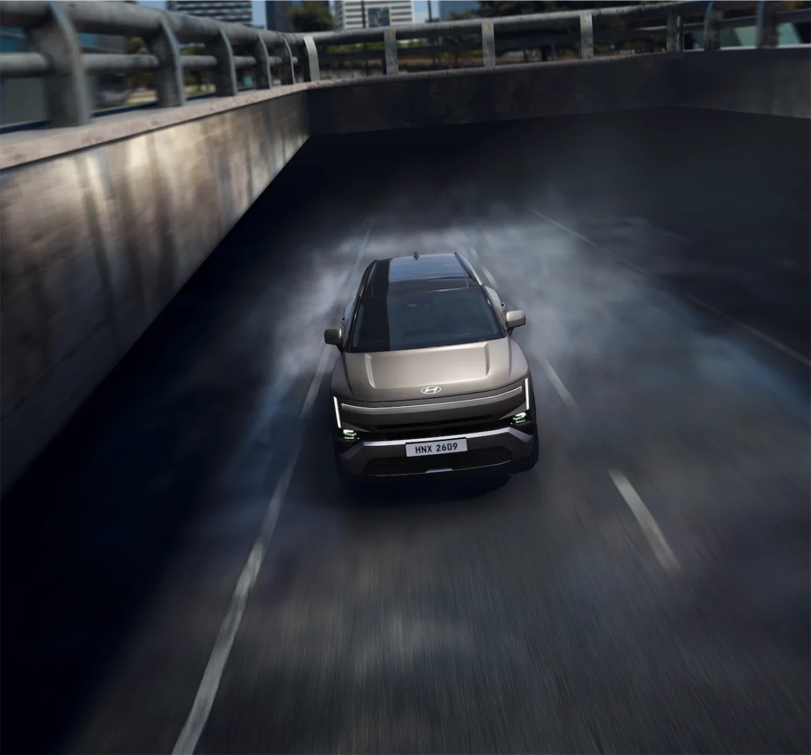 A modern Hyundai vehicle driving under a bridge, creating a cloud of smoke on the road.