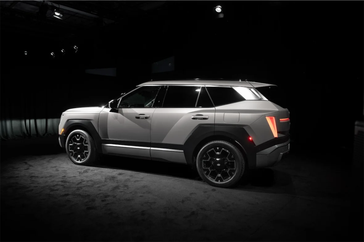 Side view of a modern SUV with a sleek design, featuring angular lines and bold wheel rims, displayed in a dimly lit environment.