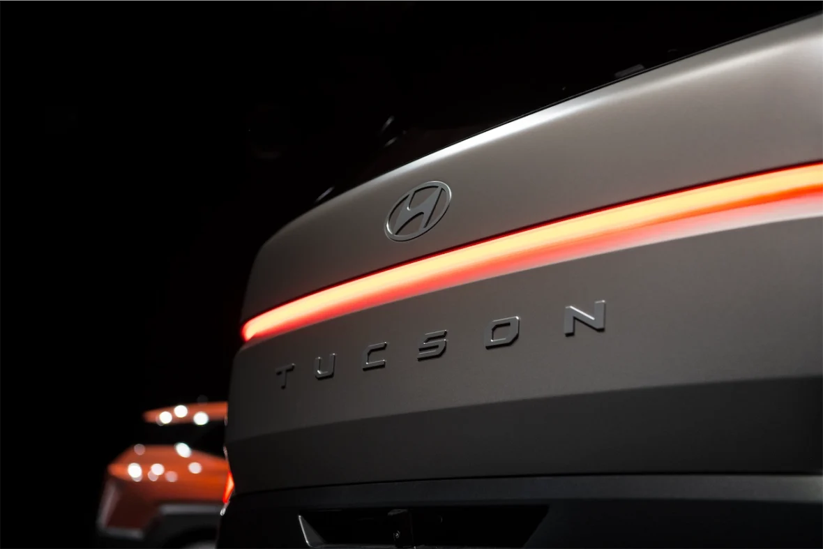 Close-up of the rear of a Hyundai Tucson, featuring the logo and the illuminated 'TUCSON' emblem against a dark background.