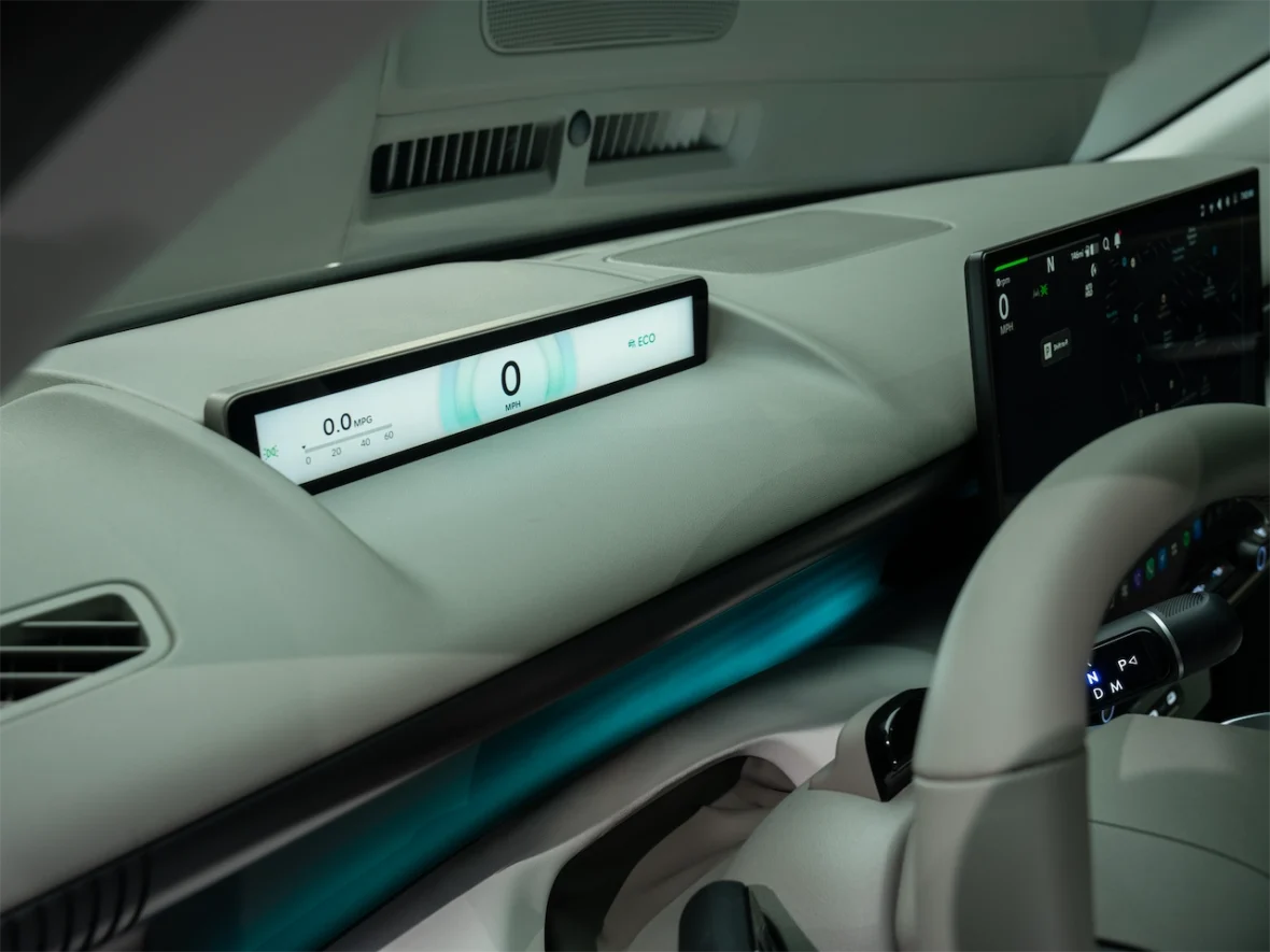 Interior view of a modern car dashboard featuring a digital speedometer display with readings of 0 MPH and 0.0 MPG, and a secondary display screen with navigation and vehicle information.