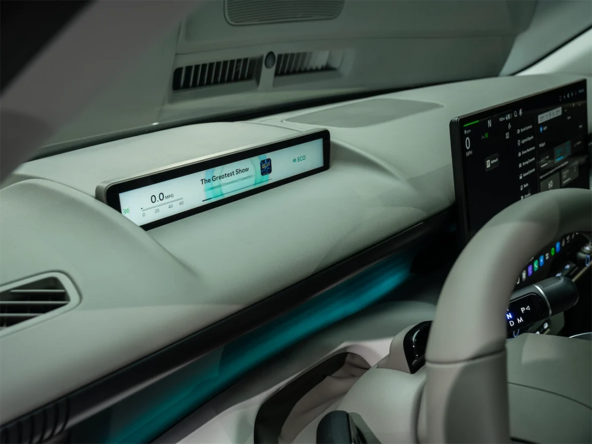 Interior dashboard of a modern vehicle featuring a digital display showing 0.0 MPG and the song 'The Greatest Show', with a sleek design and ambient lighting.