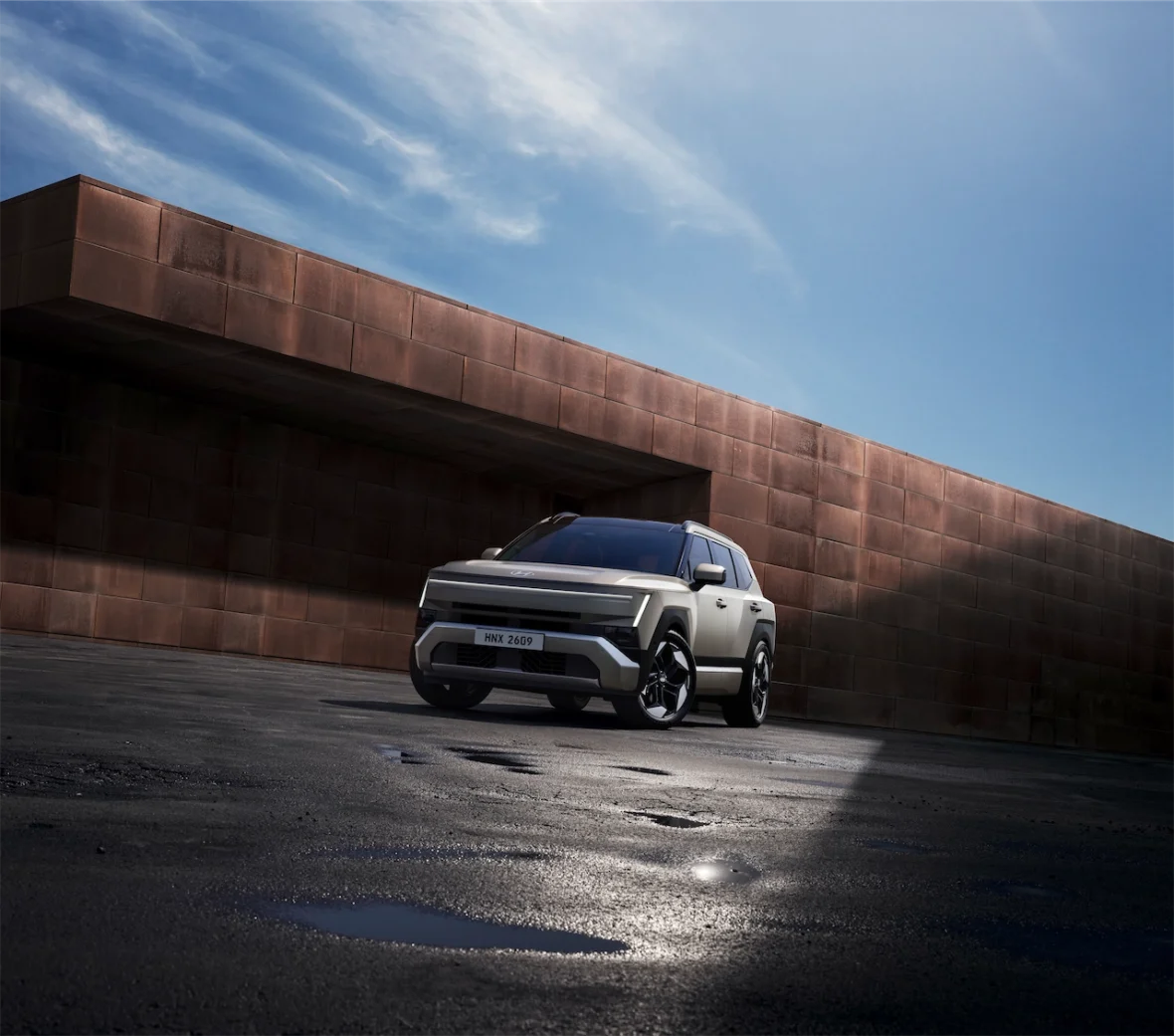 A modern SUV parked in front of a sleek, angular building with a textured copper facade under a clear blue sky.