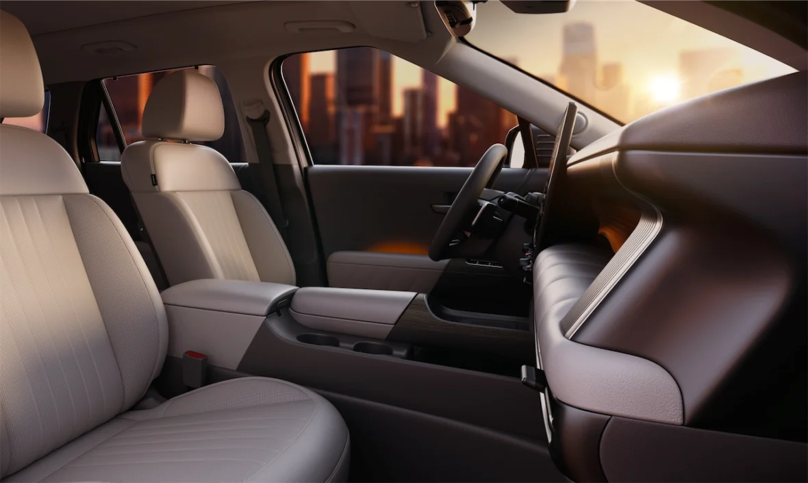 Interior view of a modern car featuring beige seats, a dashboard, and a stylish center console against a sunset backdrop.