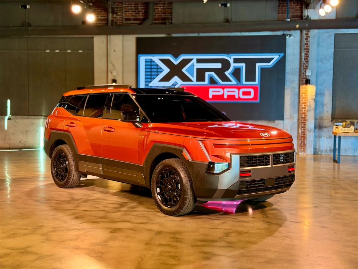 A vibrant orange SUV displayed in a modern showroom with a promotional backdrop featuring the text 'XRT PRO'.
