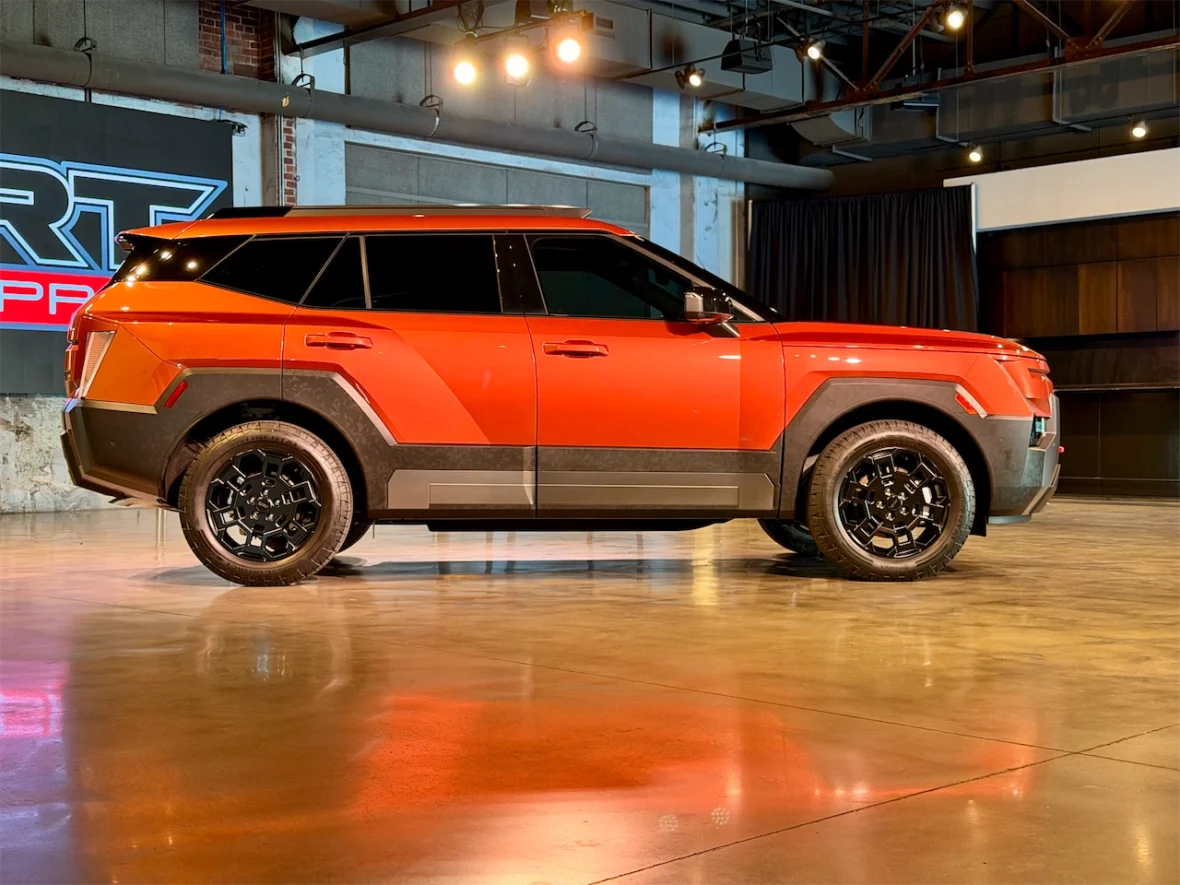 Side view of a bright orange SUV with black wheels, showcased in a well-lit indoor setting.