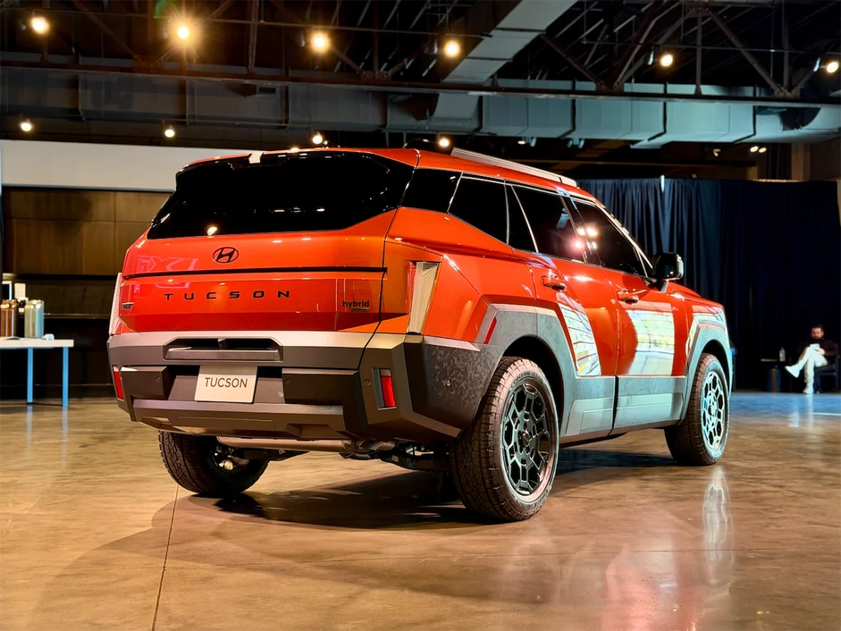 Rear view of a bright orange Hyundai Tucson hybrid parked indoors, showcasing its modern design and alloy wheels.